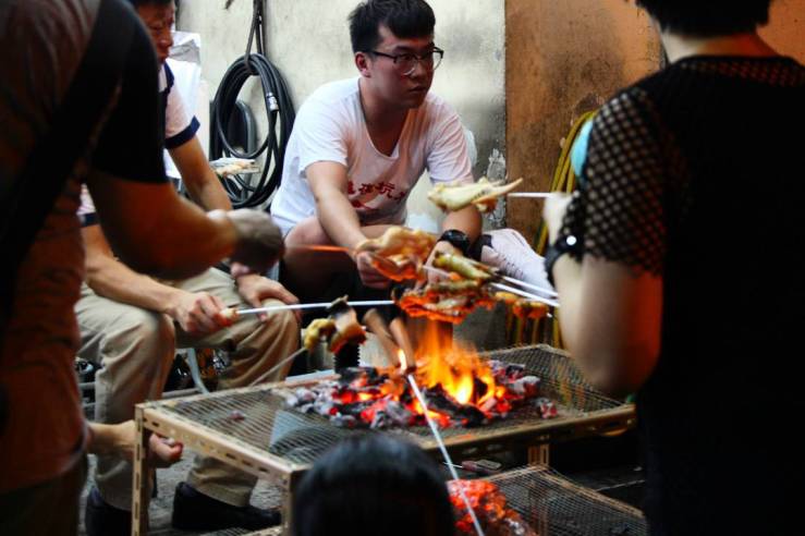 People sit around charcoal fire pit, roasting meats. Location: Tai Hang Fire Dragon Dance, Tai Hang, Hong Kong | September 27, 2015 | Tanya McGovern